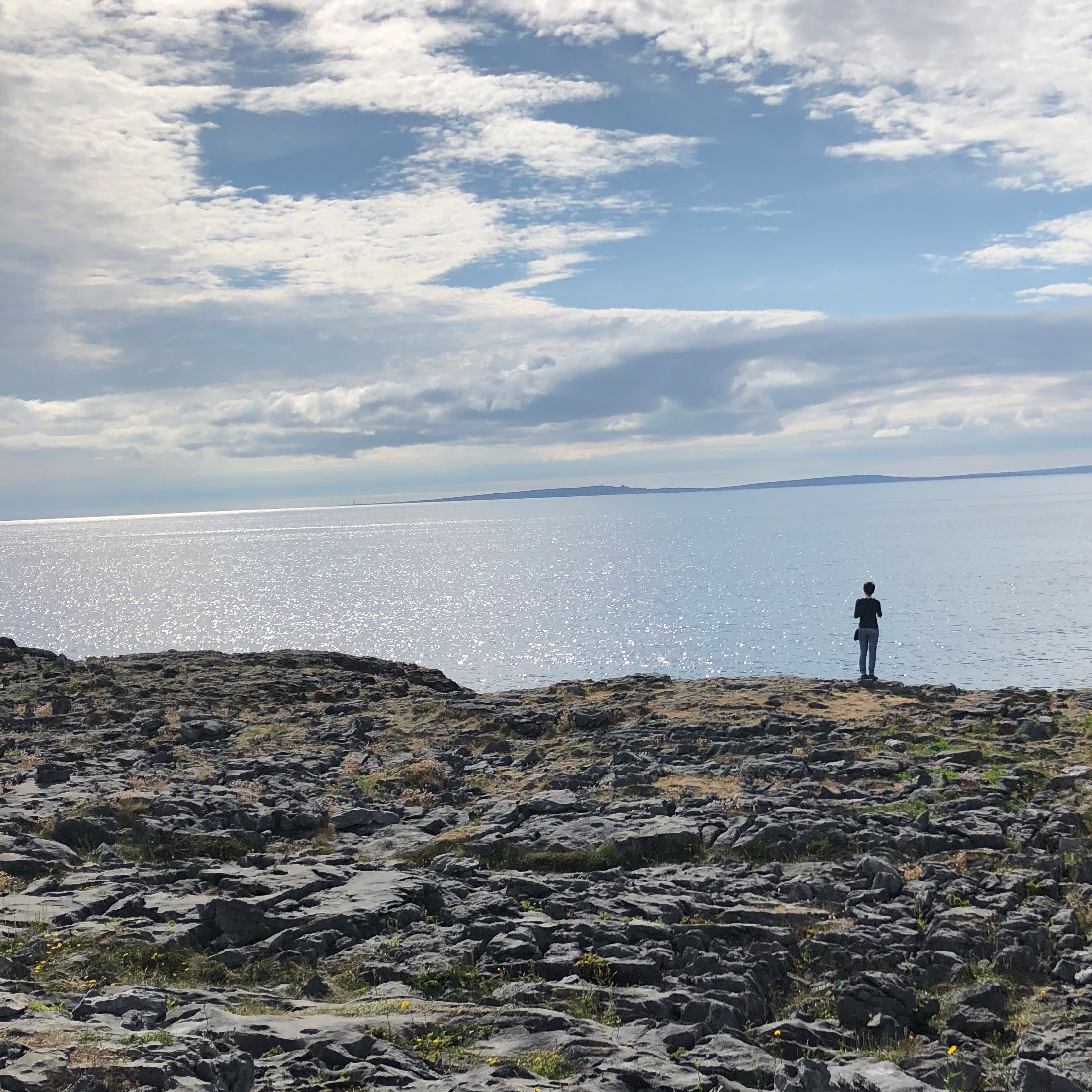 lone figure standing among large stones and staring out at sea