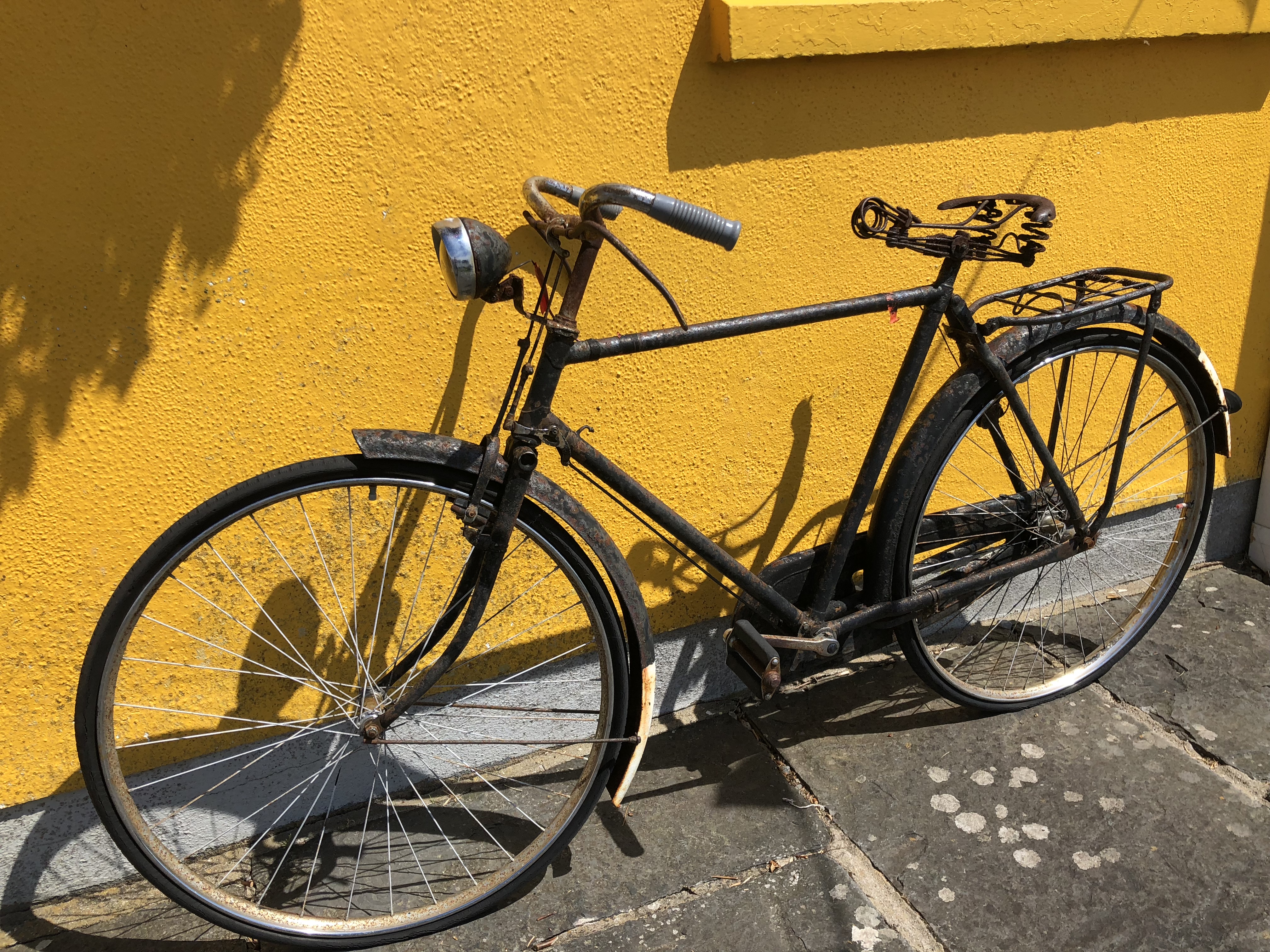 an old yellow bike leaning against the side of a building